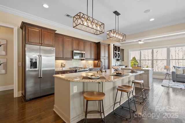 kitchen with a kitchen island with sink, stainless steel appliances, a kitchen breakfast bar, decorative backsplash, and decorative light fixtures