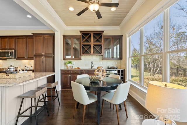 dining area featuring sink, dark wood-type flooring, ornamental molding, and a healthy amount of sunlight