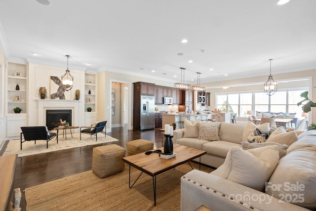 living room featuring built in shelves, sink, crown molding, a chandelier, and dark hardwood / wood-style floors