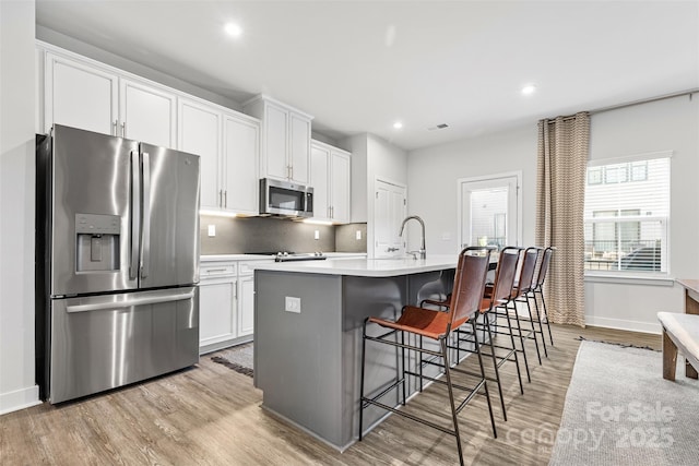 kitchen with a kitchen breakfast bar, a center island with sink, white cabinets, and appliances with stainless steel finishes