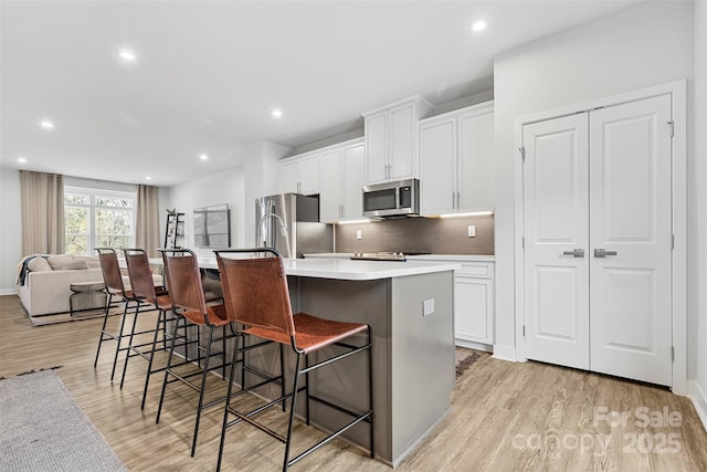 kitchen featuring stainless steel appliances, light hardwood / wood-style floors, a breakfast bar area, a kitchen island with sink, and white cabinets