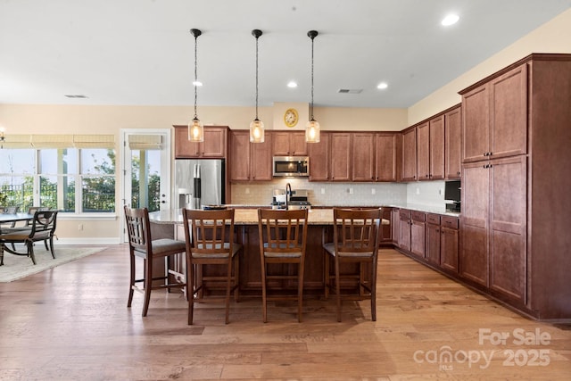 kitchen featuring decorative light fixtures, a kitchen bar, a kitchen island with sink, stainless steel appliances, and light stone countertops