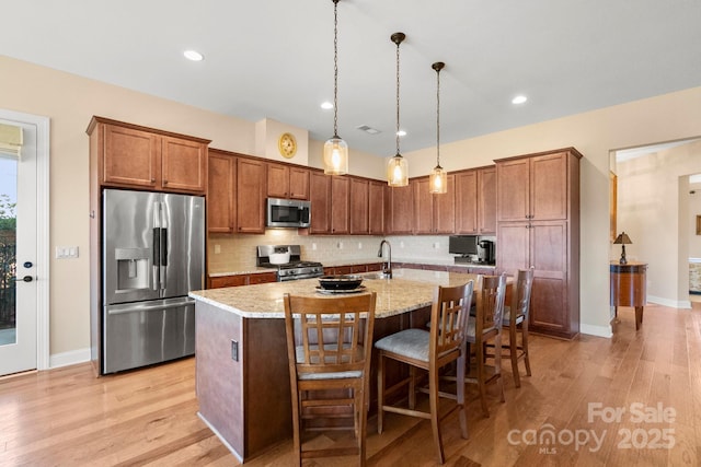 kitchen featuring a kitchen bar, hanging light fixtures, appliances with stainless steel finishes, light stone countertops, and a kitchen island with sink