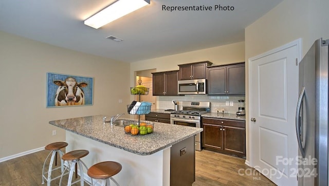 kitchen with appliances with stainless steel finishes, light wood-type flooring, dark brown cabinets, a kitchen island with sink, and a breakfast bar area