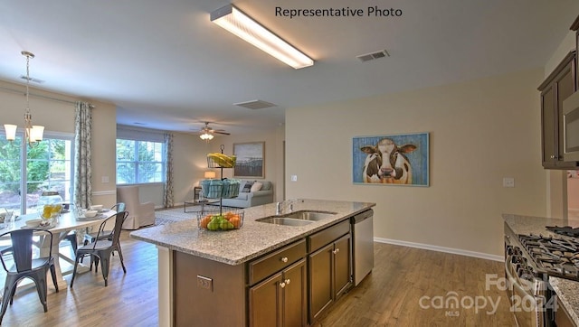 kitchen with sink, pendant lighting, a center island with sink, ceiling fan with notable chandelier, and appliances with stainless steel finishes