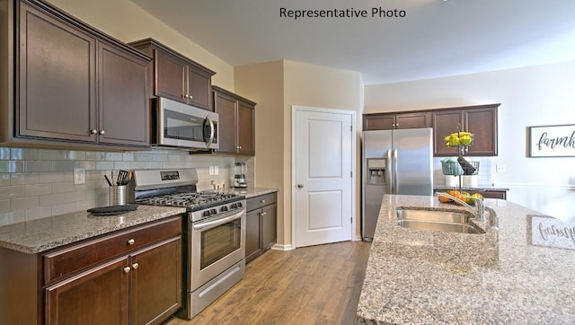 kitchen with light stone countertops, tasteful backsplash, stainless steel appliances, sink, and light hardwood / wood-style flooring