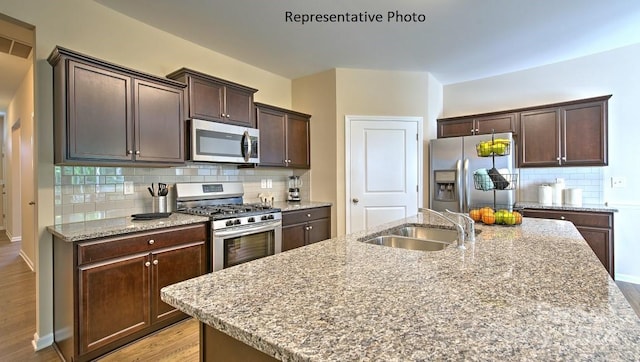 kitchen with light stone countertops, sink, stainless steel appliances, decorative backsplash, and a center island with sink