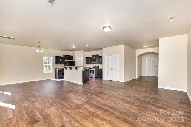 unfurnished living room with baseboards, dark wood finished floors, arched walkways, visible vents, and a notable chandelier