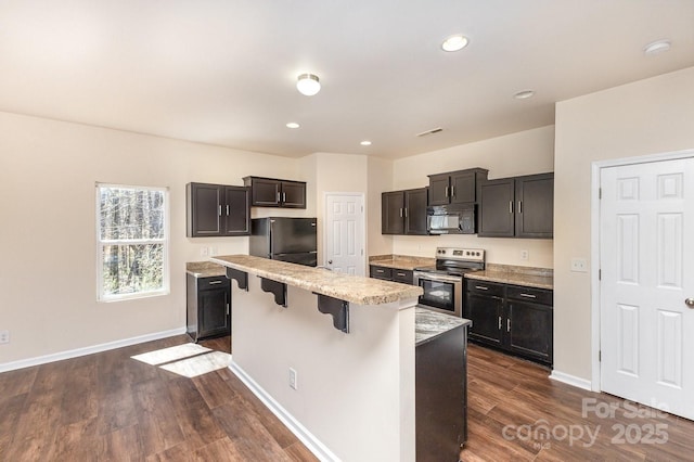 kitchen featuring a kitchen bar, baseboards, dark wood finished floors, a kitchen island, and black appliances