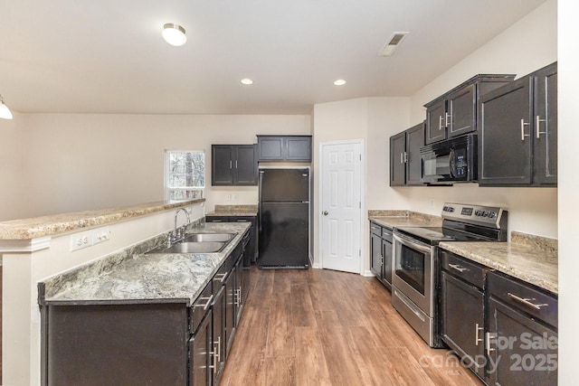 kitchen featuring a sink, an island with sink, visible vents, black appliances, and wood finished floors