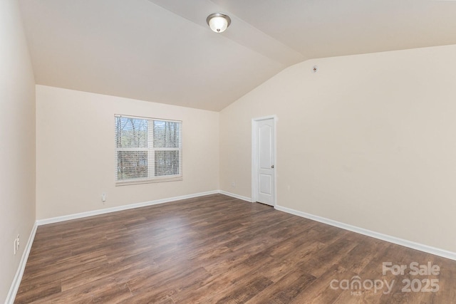 spare room featuring dark wood-style flooring, baseboards, and vaulted ceiling