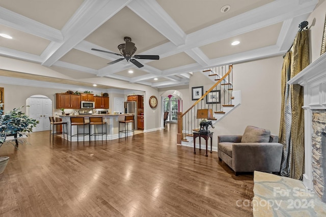 living room featuring ceiling fan, a fireplace, beamed ceiling, and coffered ceiling