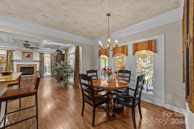 dining room featuring coffered ceiling, ceiling fan with notable chandelier, a stone fireplace, a wealth of natural light, and beamed ceiling