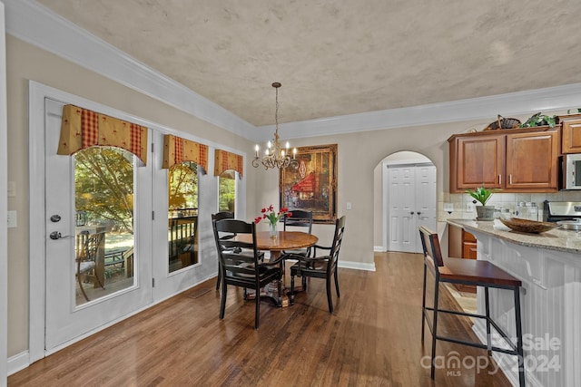 dining space with ornamental molding, dark wood-type flooring, and an inviting chandelier