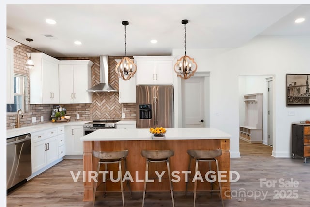 kitchen featuring stainless steel appliances, a kitchen island, white cabinets, and wall chimney range hood