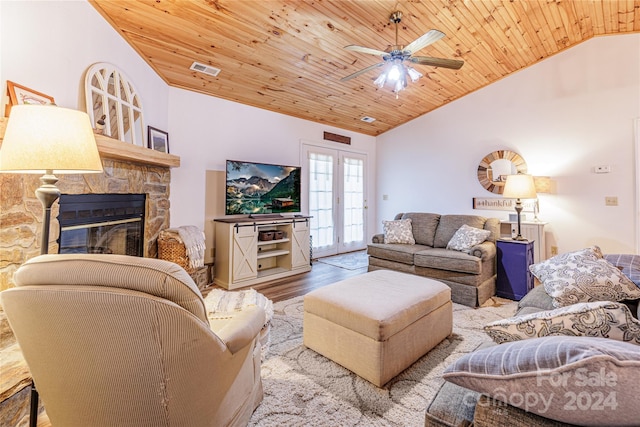 living room featuring wood ceiling, ceiling fan, light hardwood / wood-style floors, a stone fireplace, and lofted ceiling