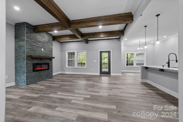 unfurnished living room featuring hardwood / wood-style floors, a stone fireplace, sink, beamed ceiling, and a notable chandelier