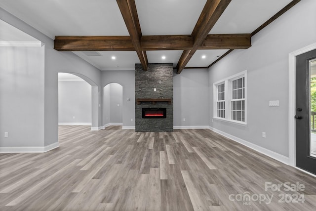 unfurnished living room featuring ornamental molding, coffered ceiling, beam ceiling, light hardwood / wood-style flooring, and a stone fireplace