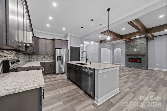 kitchen with pendant lighting, a center island with sink, a stone fireplace, appliances with stainless steel finishes, and beamed ceiling