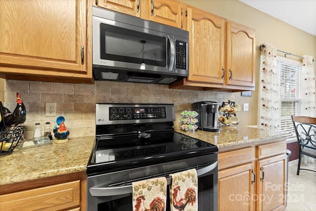 kitchen with appliances with stainless steel finishes, tasteful backsplash, light stone counters, and light tile patterned flooring