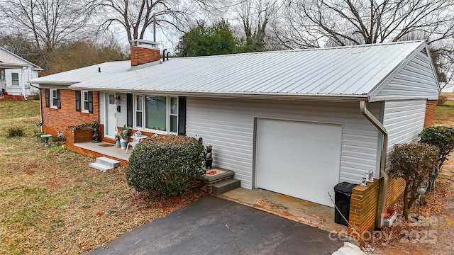 ranch-style home with a chimney, covered porch, an attached garage, metal roof, and driveway