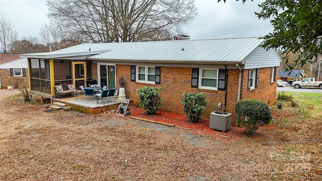 rear view of house with brick siding, a chimney, a sunroom, metal roof, and cooling unit