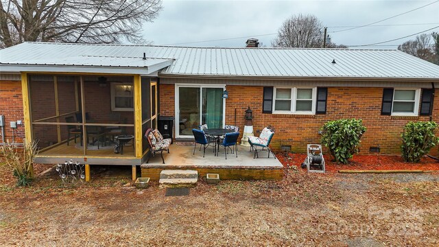 back of house with brick siding, a sunroom, a patio area, metal roof, and crawl space