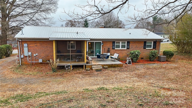 rear view of property with a sunroom, crawl space, brick siding, and metal roof