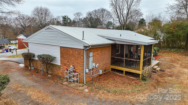 rear view of property featuring a garage, metal roof, brick siding, and a sunroom