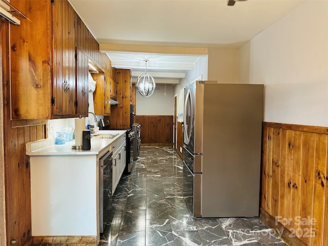 kitchen featuring marble finish floor, a wainscoted wall, appliances with stainless steel finishes, wood walls, and a sink