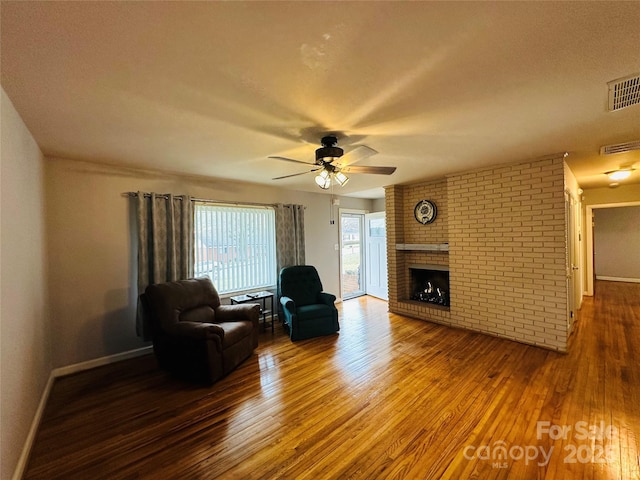 living area featuring a fireplace, wood finished floors, visible vents, and baseboards