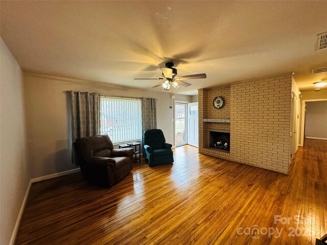 living area featuring baseboards, visible vents, a ceiling fan, wood-type flooring, and a fireplace