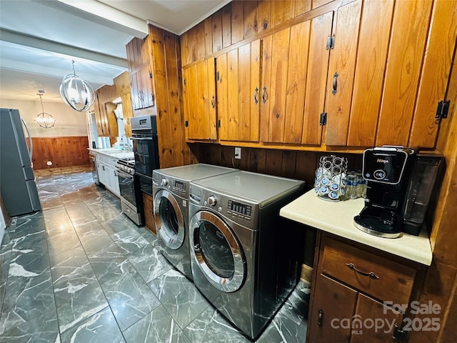 clothes washing area featuring wooden walls, laundry area, marble finish floor, independent washer and dryer, and wainscoting