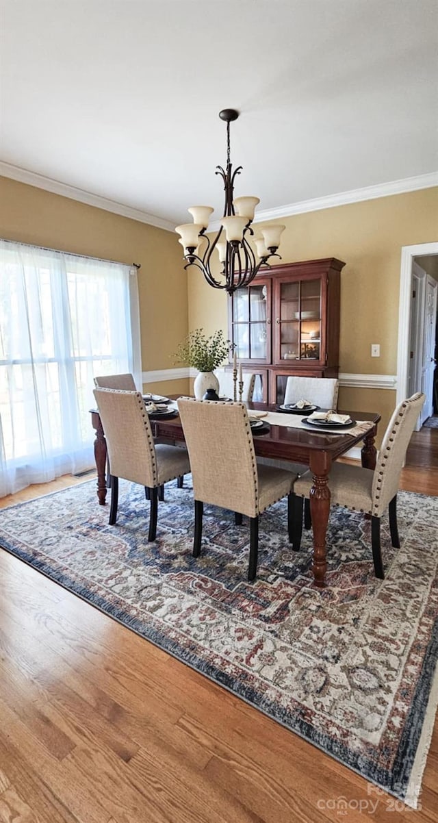 dining area featuring crown molding, wood-type flooring, and an inviting chandelier