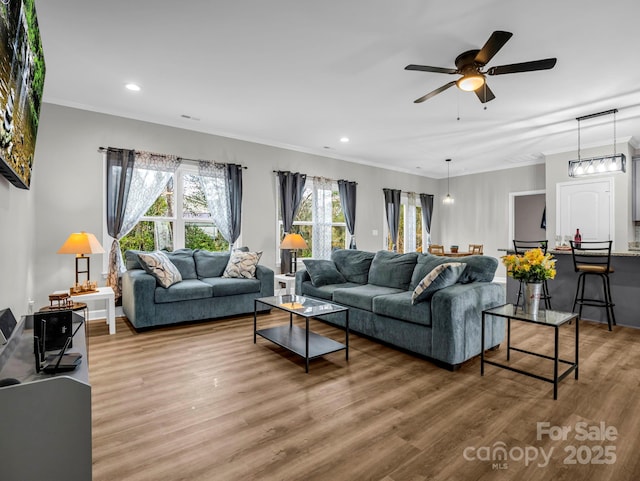 living area with recessed lighting, wood finished floors, visible vents, and crown molding