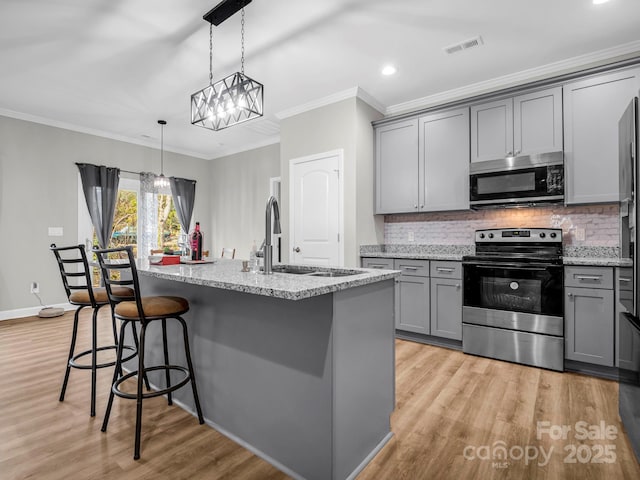 kitchen with appliances with stainless steel finishes, an island with sink, sink, hanging light fixtures, and crown molding