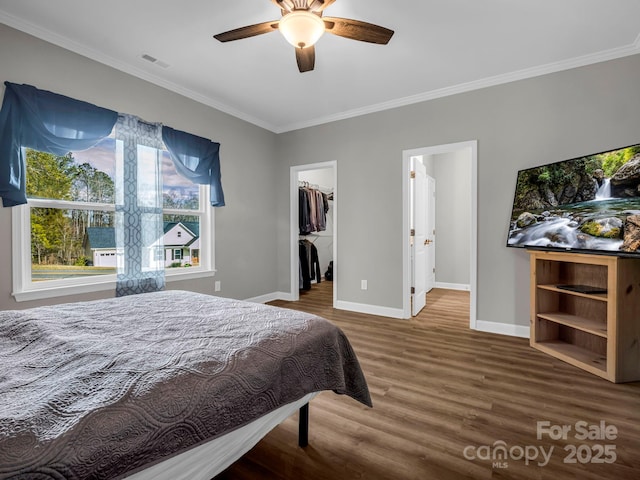 bedroom with a walk in closet, ornamental molding, a closet, hardwood / wood-style flooring, and ceiling fan