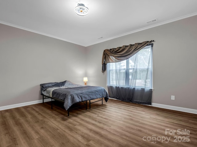 bedroom featuring baseboards, visible vents, crown molding, and wood finished floors