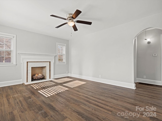 unfurnished living room with ceiling fan, a fireplace, and dark wood-type flooring