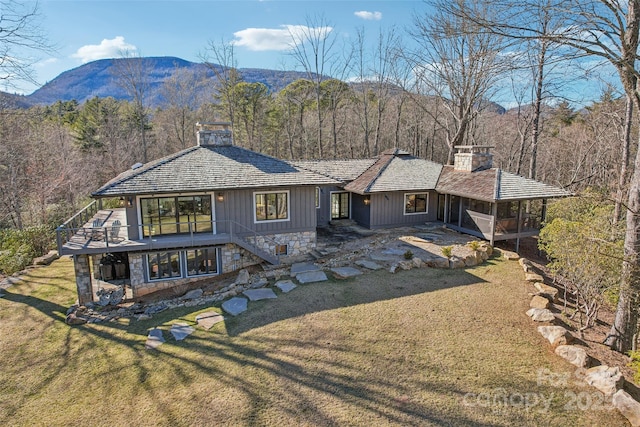 rear view of property with stairs, a yard, driveway, a chimney, and a wooded view