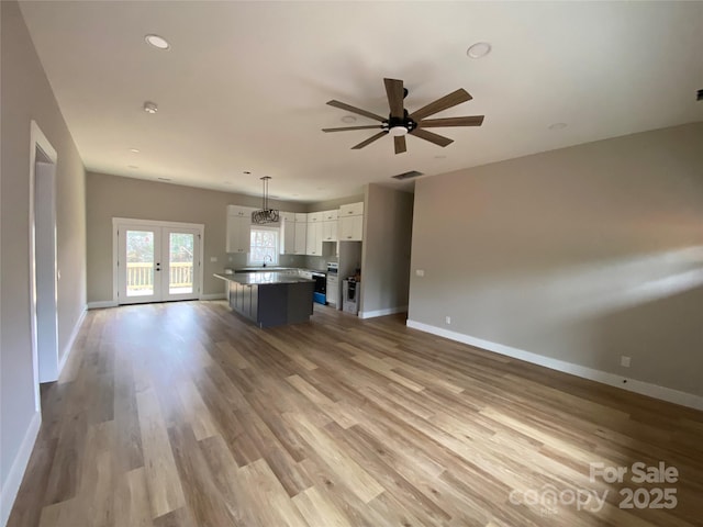 unfurnished living room with a ceiling fan, wood finished floors, baseboards, and french doors