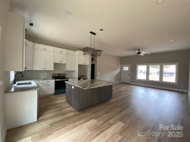 kitchen featuring light wood-type flooring, electric stove, a sink, a kitchen island, and white cabinetry