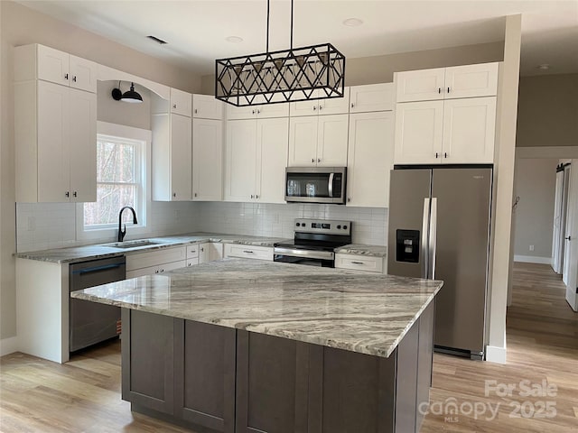 kitchen with a sink, stainless steel appliances, light stone countertops, and white cabinetry