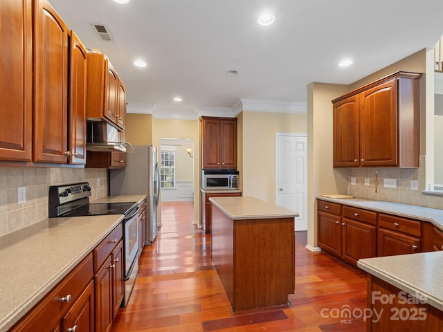 9903 Southampton Commons Dr, Charlotte, NC 28277 - kitchen with stainless steel appliances, wood finished floors, under cabinet range hood, ornamental molding, and a center island