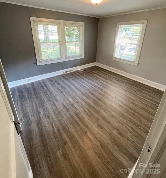 empty room with dark hardwood / wood-style floors, a wealth of natural light, and ornamental molding