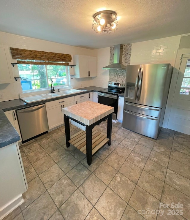 kitchen featuring tasteful backsplash, wall chimney exhaust hood, a textured ceiling, stainless steel appliances, and white cabinets