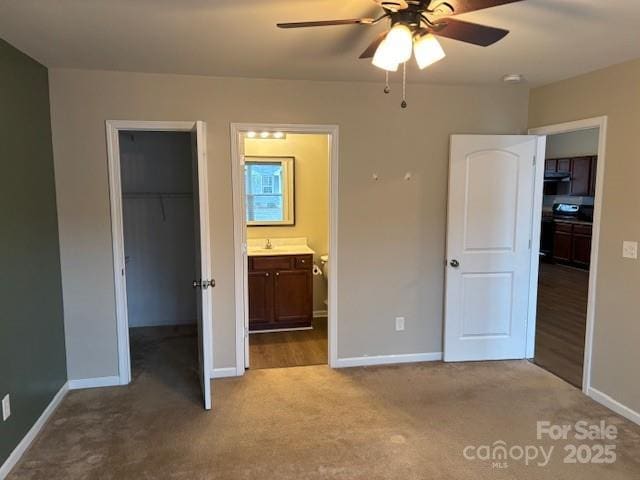 unfurnished bedroom featuring light colored carpet, ceiling fan, a spacious closet, connected bathroom, and a closet