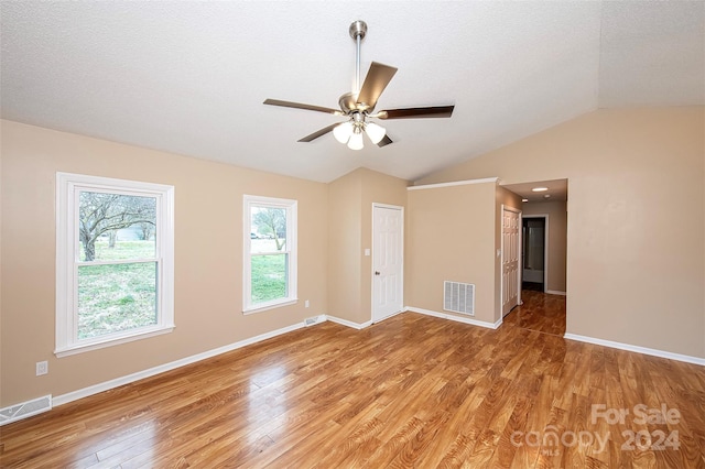 empty room with a textured ceiling, ceiling fan, light hardwood / wood-style flooring, and lofted ceiling