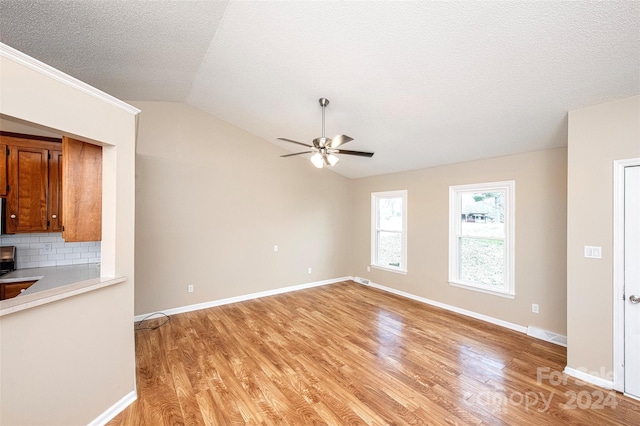 unfurnished living room featuring ceiling fan, light wood-type flooring, a textured ceiling, and vaulted ceiling