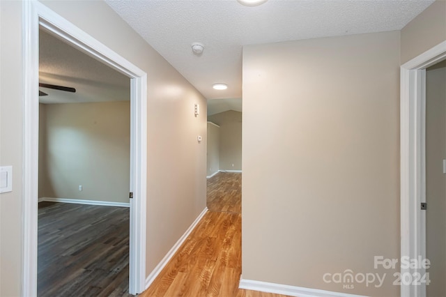 hall with hardwood / wood-style floors, a textured ceiling, and vaulted ceiling